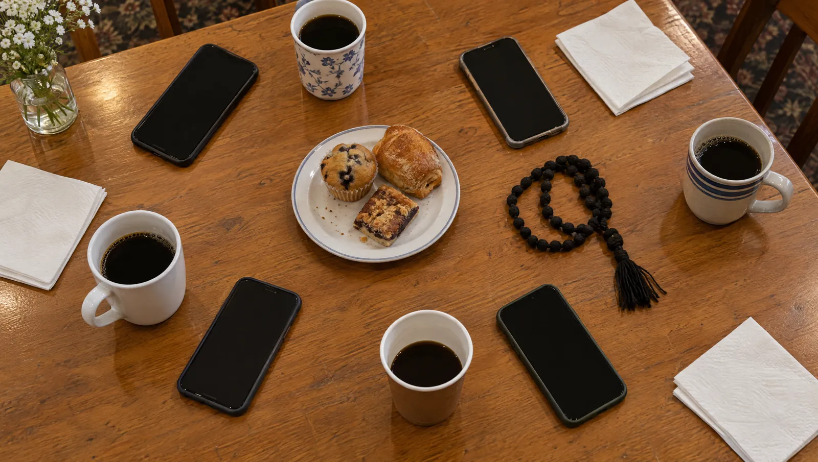 Phones, coffee cups, pastries and a prayer rope on a parish hall table